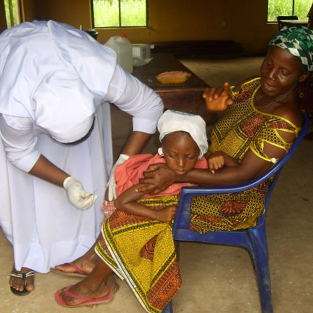 Eine Ärztin, Dr. Joyce Ezeugo, gibt in einem Slum in Okpoko, Nigeria, einem Mädchen eine Spritze. Das Mädchen wird von seiner Mutter auf einem blauen Plastikstuhl festgehalten.