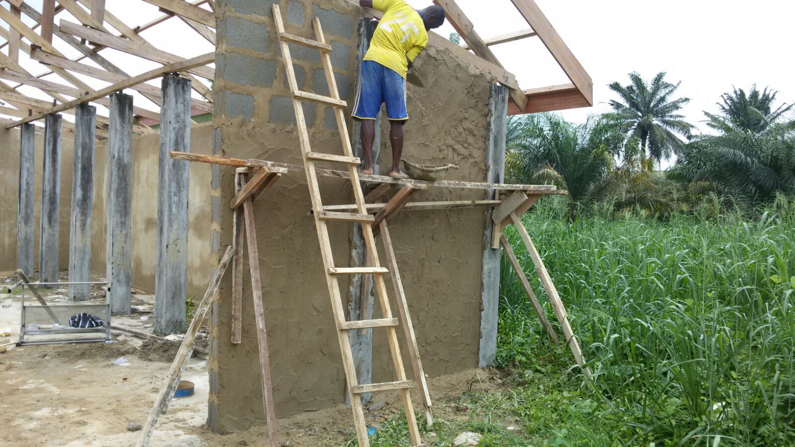 Ein Bauarbeiter in Schutzkleidung zieht eine Wand hoch bei dem Rohbau der neuen Schule in Calabar, Nigeria. Im Hintergrund ist ein weiterer Bauarbeiter zu sehen und im Vordergrund ist das Fundament der Schule erkennbar.