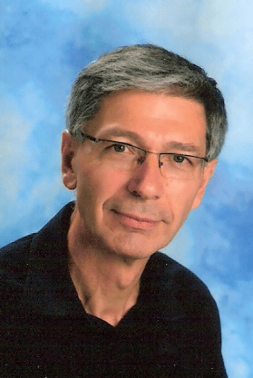 Uwe Kraus, Präsident von HIFA - Hilfe für alle, sitzt auf einem Stuhl und lächelt in die Kamera.