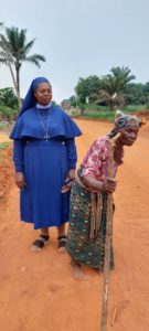 Sr. Joyce und ihre Mutter stehen auf sandiger Straße und kochen Palmöl