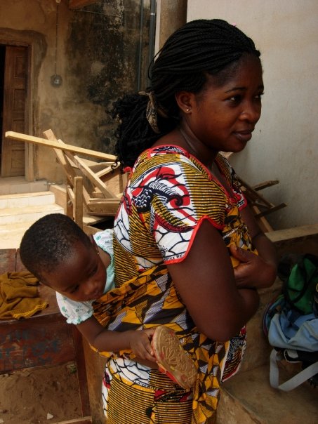 Nigerianische Mutter mit Baby auf dem Rücken in traditionellem afrikanischem Kleid lächelt